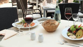 Un tavolo da pranzo all'aperto con piatti di cibo, bicchieri di vino e condimenti.