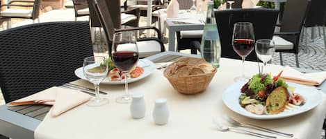 Una mesa de comedor al aire libre con platos de comida, copas de vino y saleros.