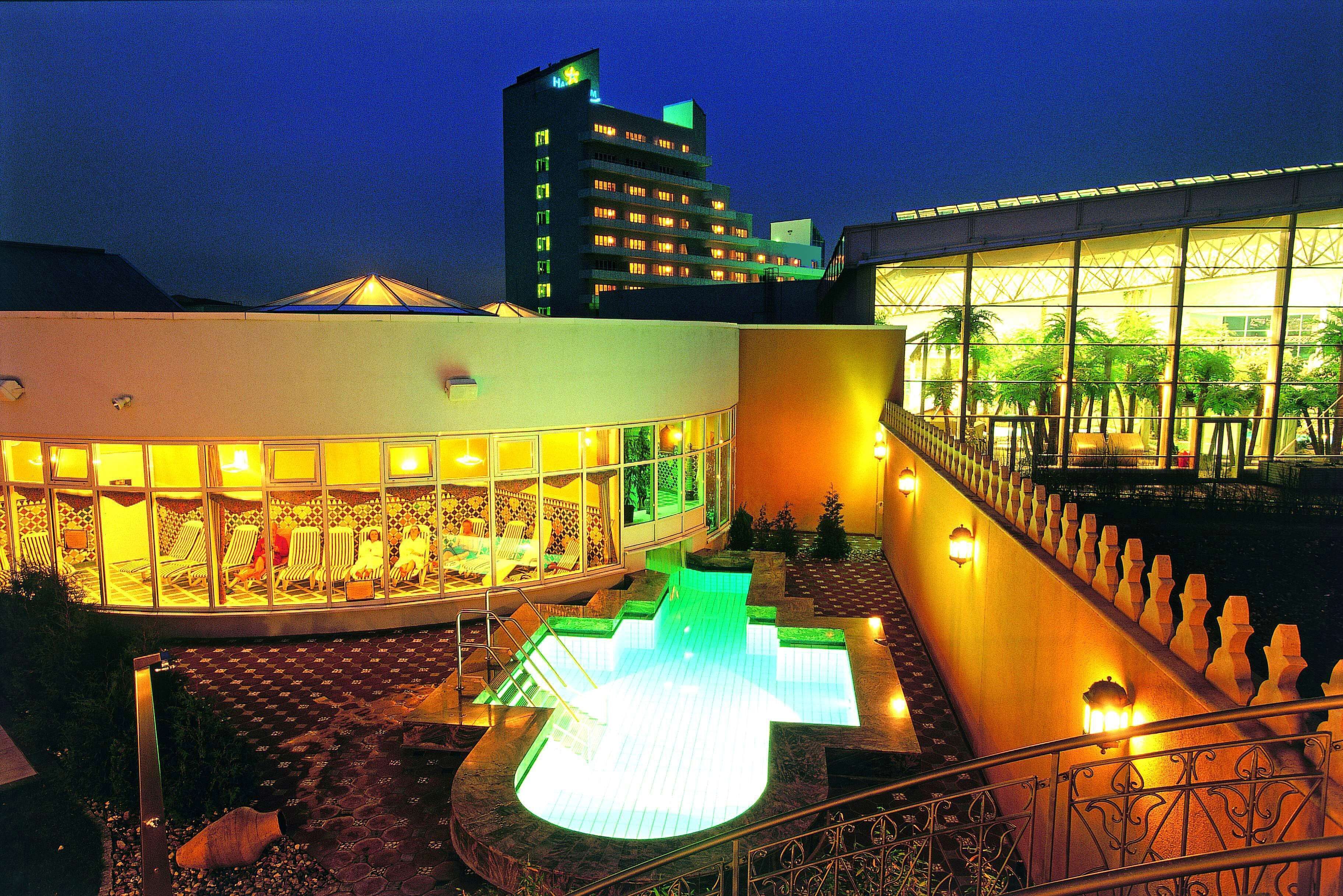 A hotel with a swimming pool, outdoor seating, and a view of a tall building in the background.