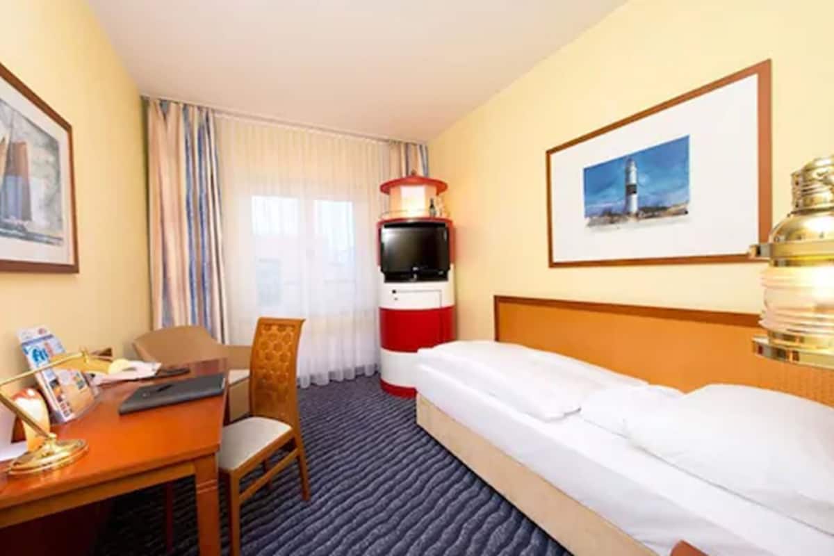 A hotel room with a bed, a desk with a chair, a television, a lamp, and a framed picture on the wall.