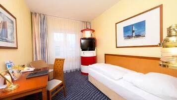 A hotel room with a bed, a desk with a chair, a television, a lamp, and a framed picture on the wall.