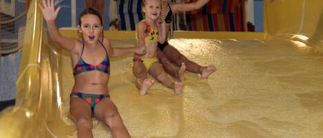 Children sliding down a water slide in a pool area.
