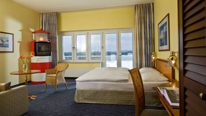 A hotel room with a bed, a small table with a vase, a chair, a television, and a window with a view of the outside.