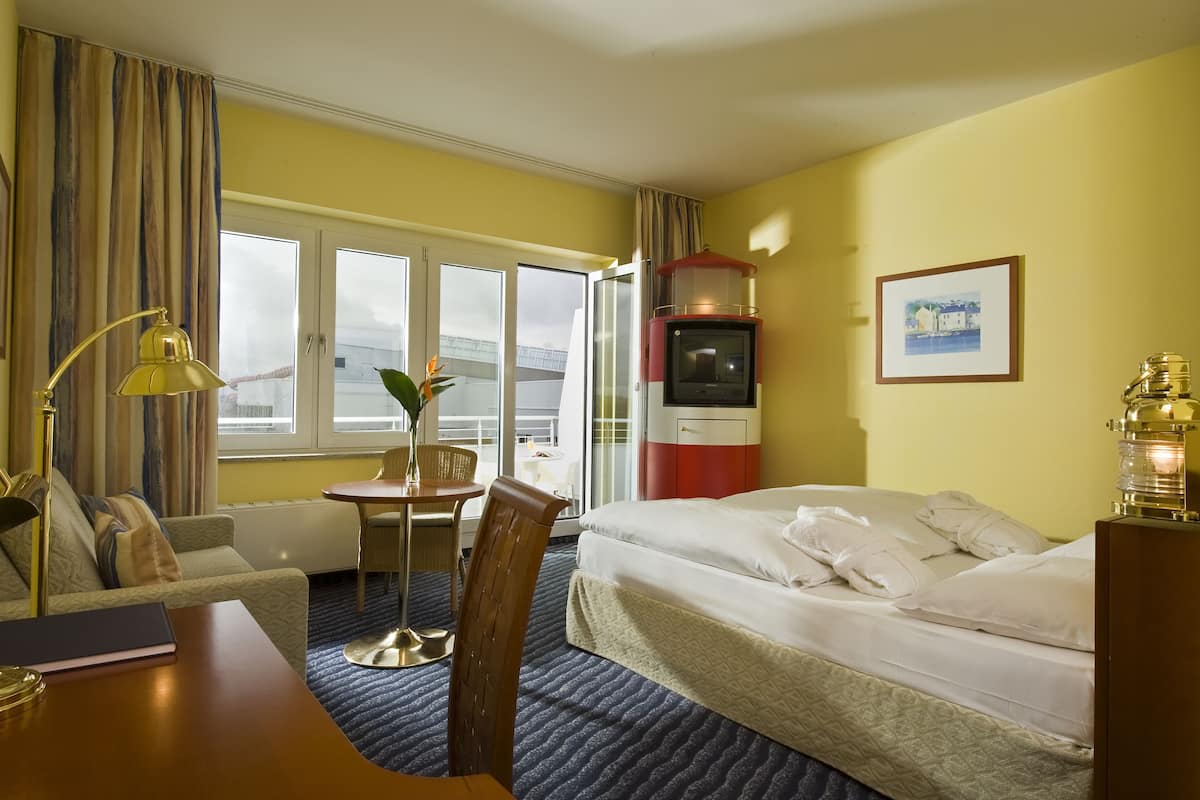 Une chambre d’hôtel avec un lit, un bureau, une chaise, une petite table avec un vase, une télévision et une fenêtre avec des rideaux.