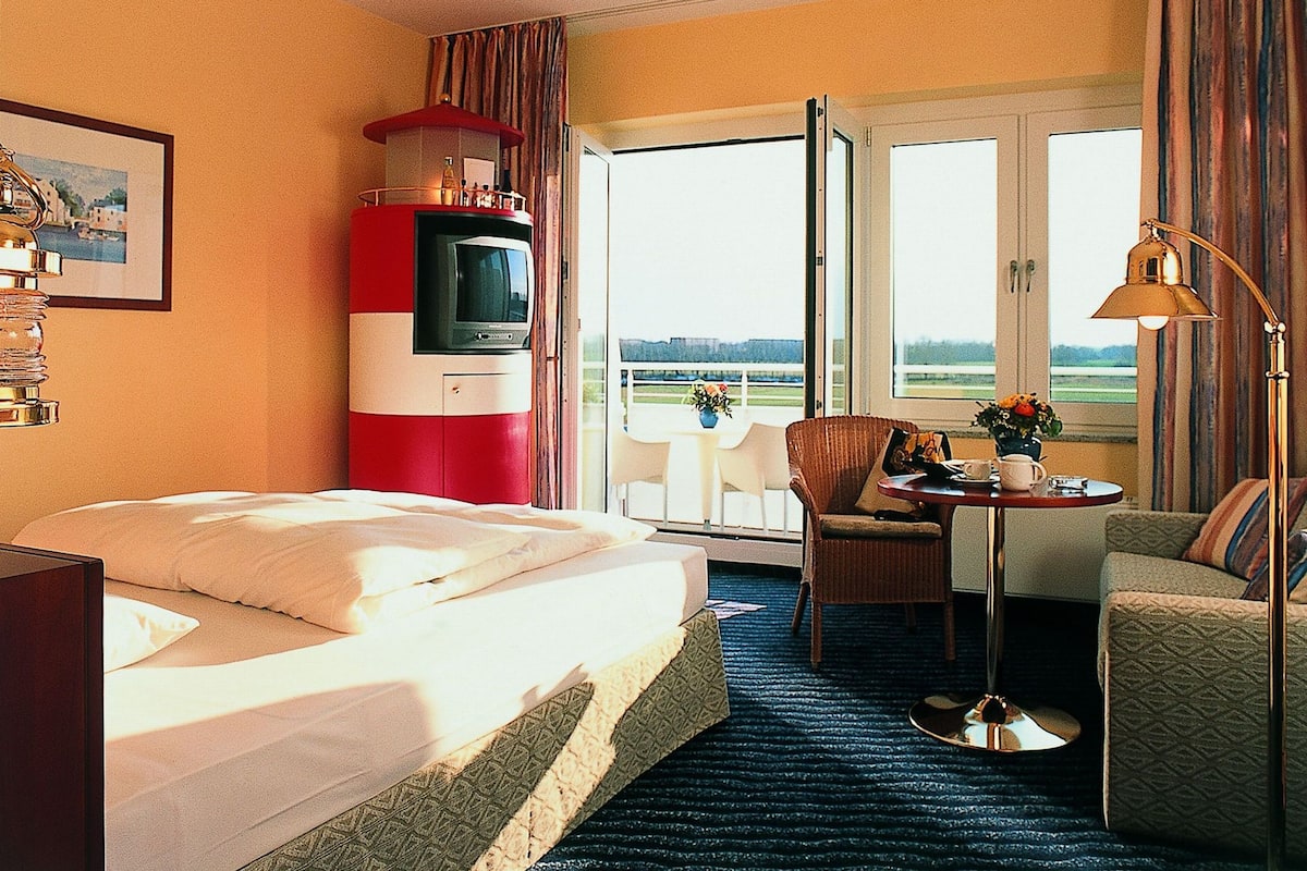 Une chambre d’hôtel comprenant un lit, une télévision, un balcon avec une chaise et une table, et donnant sur l’extérieur.