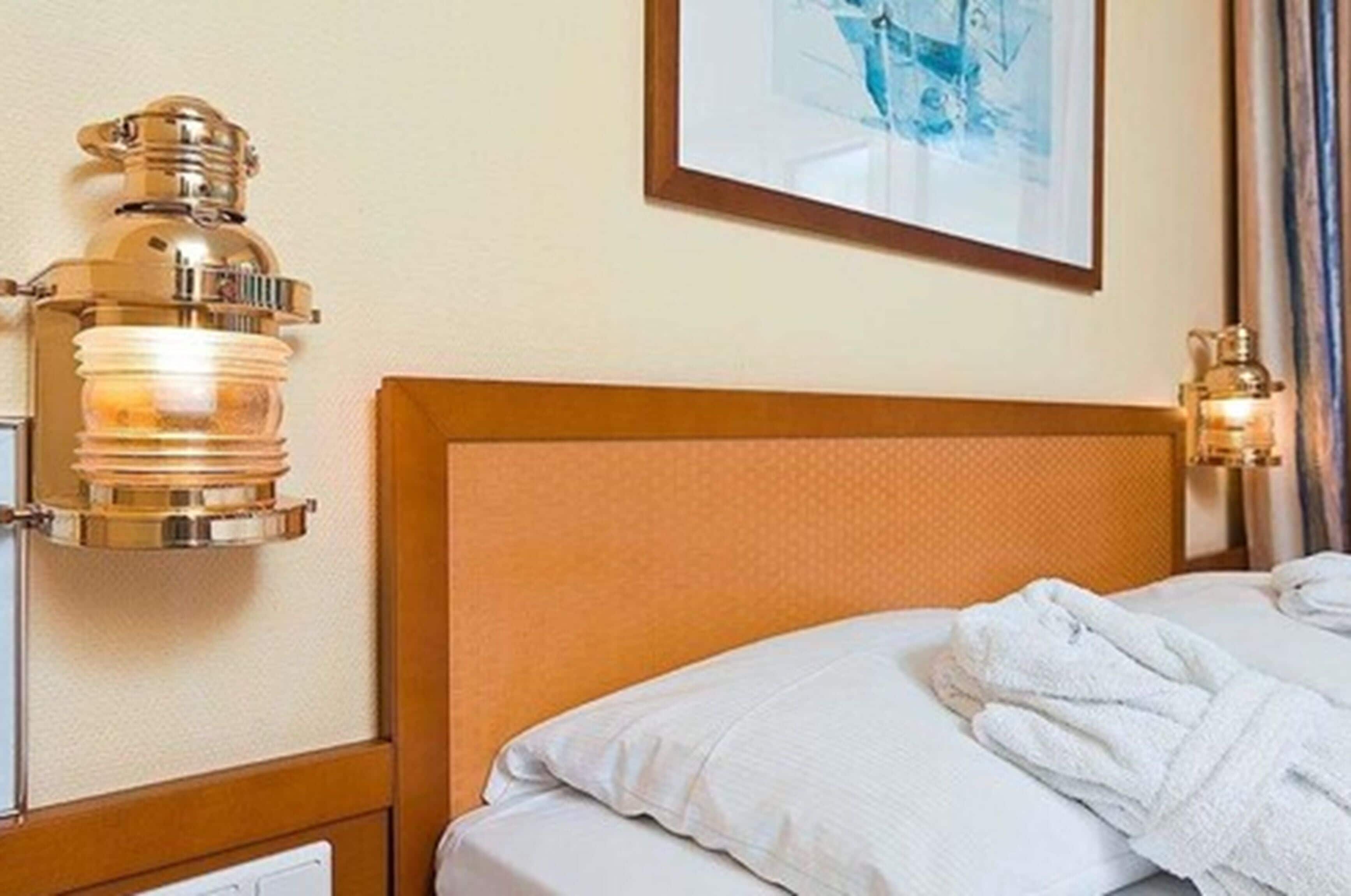 A hotel room with a wooden headboard, a framed picture on the wall, and two wall-mounted lamps.