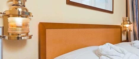A hotel room with a wooden headboard, a framed picture on the wall, and two wall-mounted lamps.