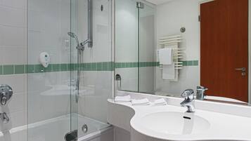 Uma casa de banho moderna com cabine de duche em vidro, lavatório branco com espelho e porta de madeira.