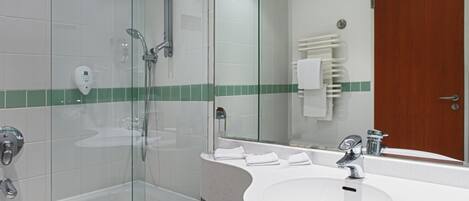 Un baño moderno con ducha de vidrio, un lavamanos blanco con espejo y una puerta de madera.