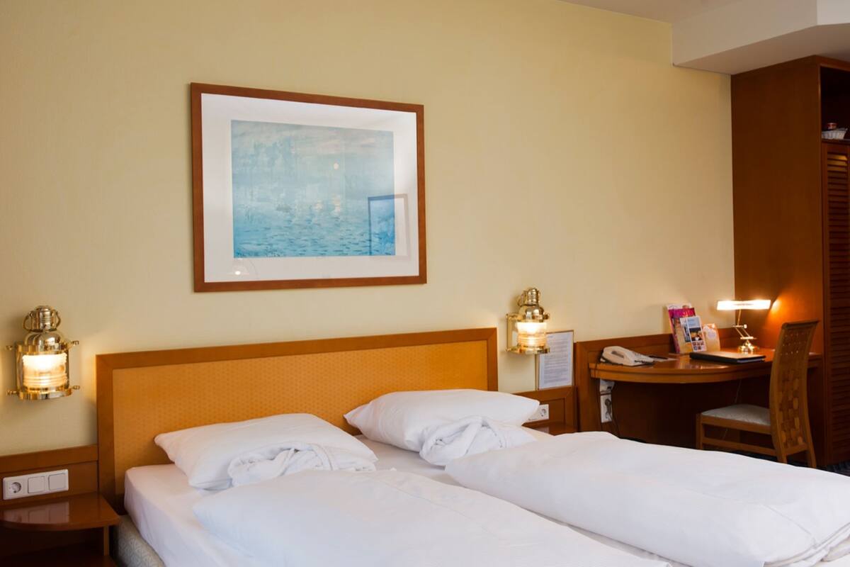 Une chambre d’hôtel avec un grand lit, deux tables de chevet, un bureau avec une chaise, un tableau encadré au mur et une armoire.