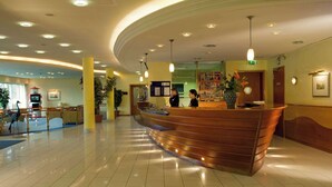 A hotel reception area with a curved wooden reception desk, multiple ceiling lights, and a reception desk with a computer and telephone.
