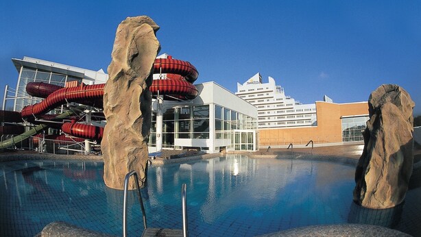A swimming pool with rock formations, a water slide, and a modern building with a large glass facade.