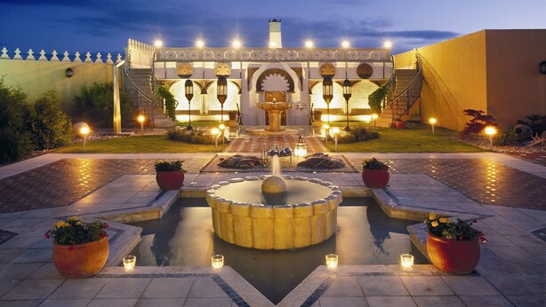 A courtyard with a central fountain, surrounded by potted plants and a staircase leading to a building with traditional architectural elements.