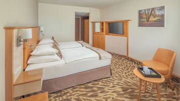 A hotel room with a bed, a chair, a small table, and a painting on the wall.
