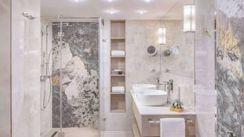 Un baño moderno con ducha de vidrio, paredes de mármol y tocador doble.