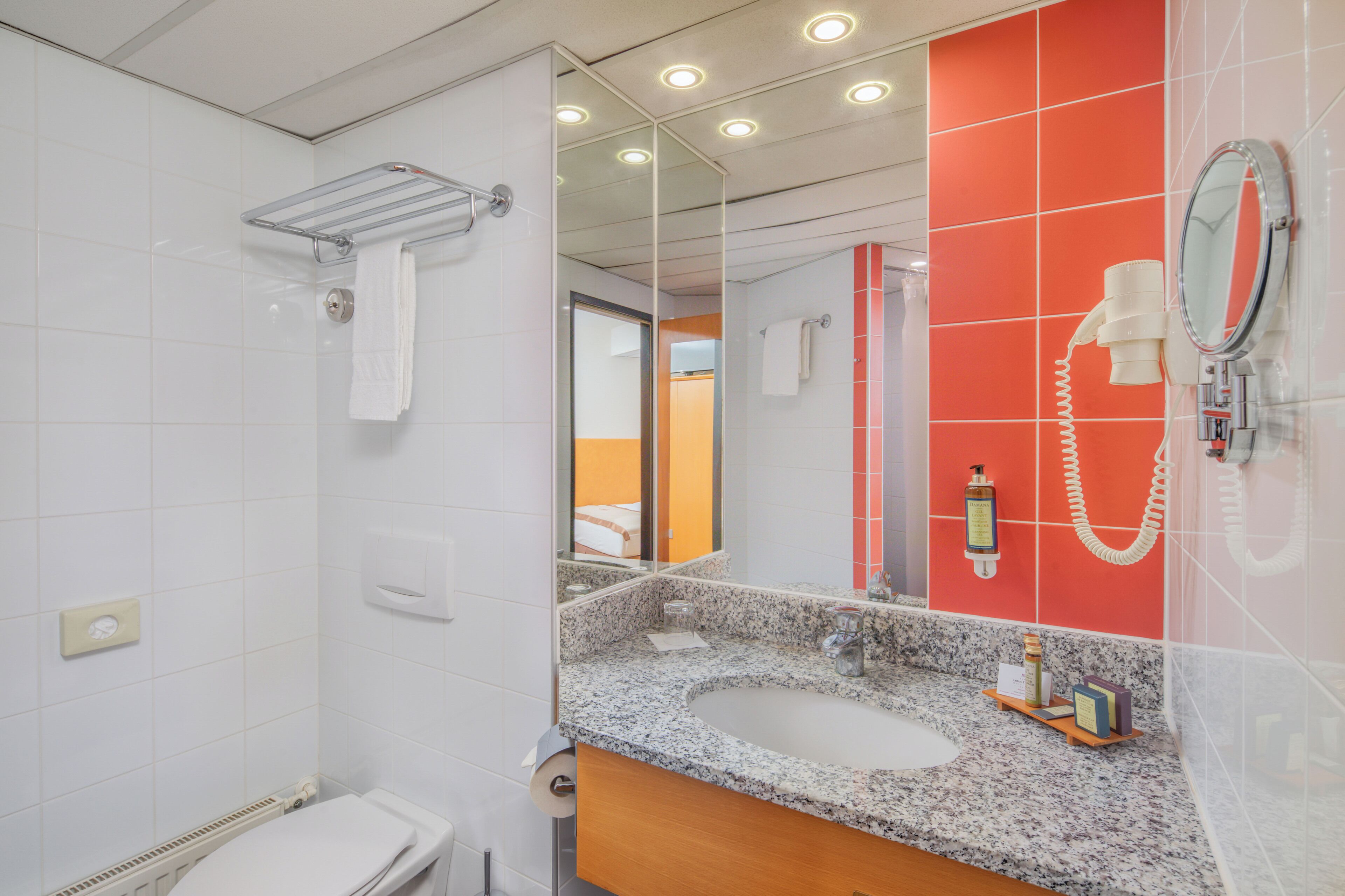 A bathroom with a white toilet, a shower, a sink with a mirror, and a red accent wall.