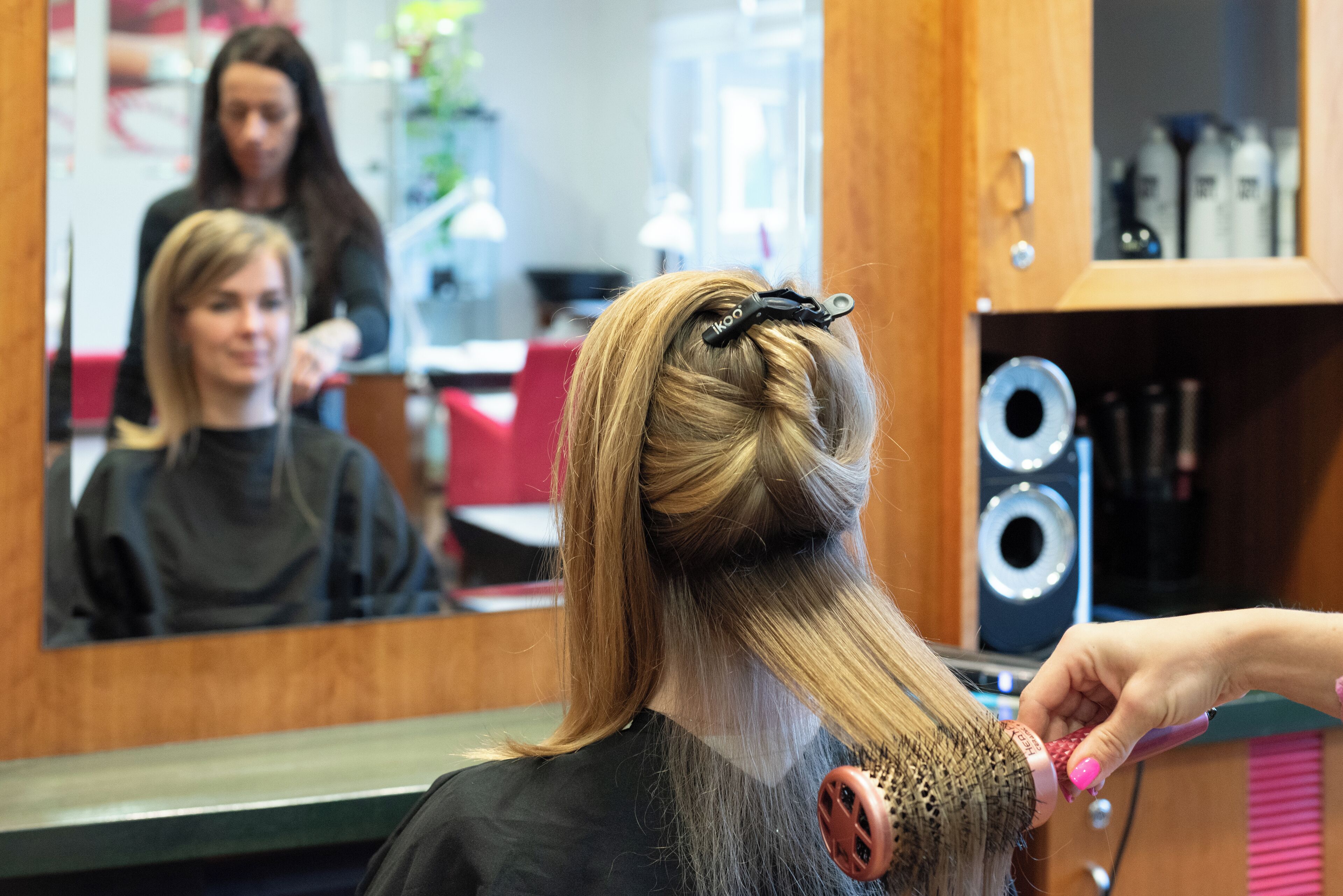 L'intérieur d'un salon de coiffure, avec un miroir, un sèche-cheveux et une personne qui coiffe.