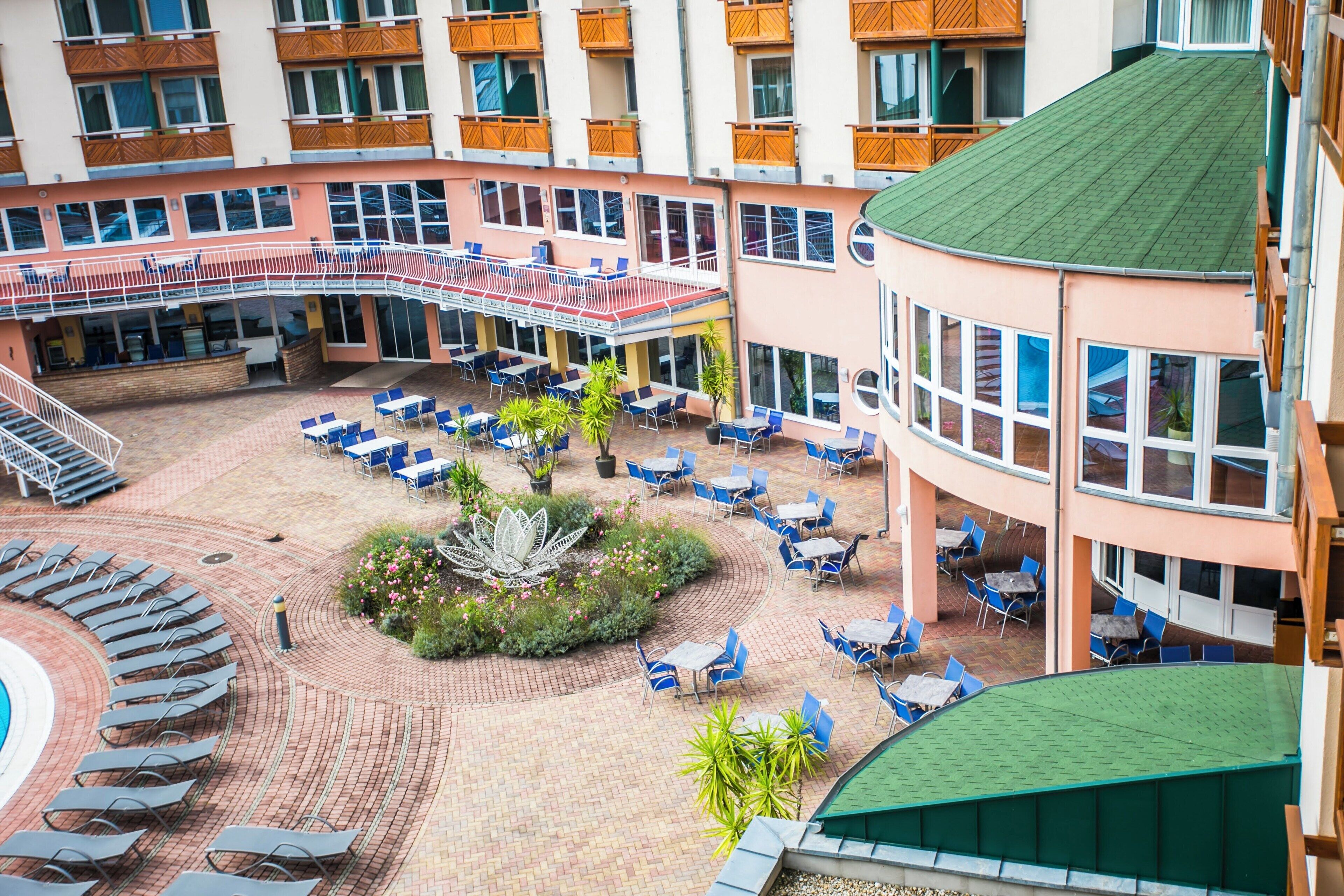 A hotel courtyard with outdoor seating, a pool, and multiple balconies.