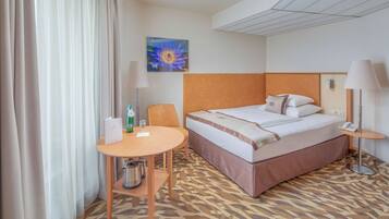 Hotelkamer met een bed, een klein tafeltje met stoel, een lamp, een schilderij aan de muur en een kamerbreed tapijt met dessin.