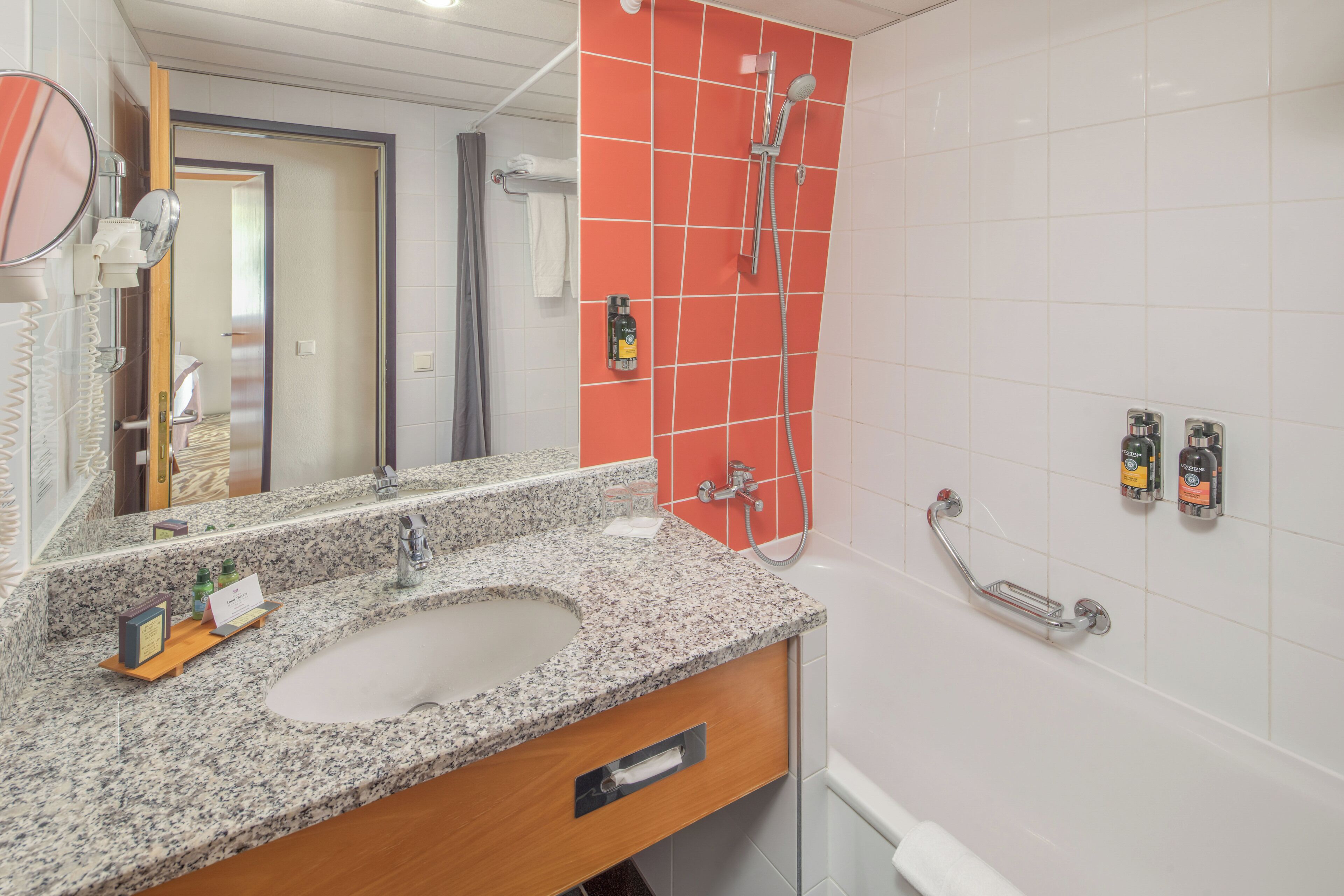 A bathroom with a granite countertop sink, a mirror, a shower with a handheld showerhead, and a towel rack.