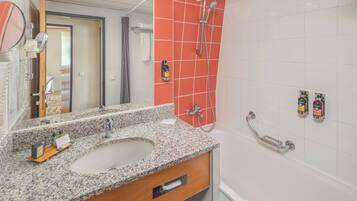 Un baño con lavamanos de encimera de granito, espejo, ducha con cabezal de ducha manual y toallero.
