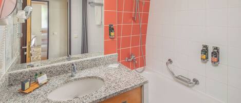 A bathroom with a granite countertop sink, a mirror, a shower with a handheld showerhead, and a towel rack.