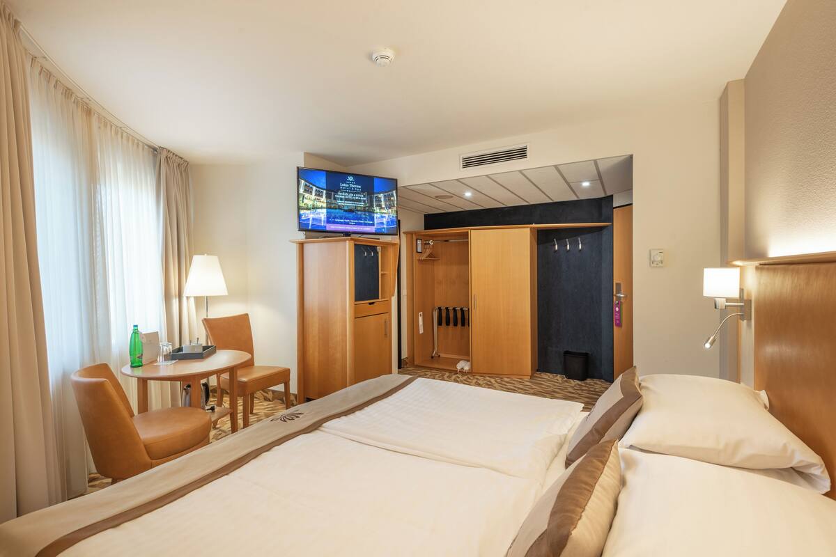 Ein Hotelzimmer mit zwei Betten, einem Fernseher, einem Schreibtisch mit Stuhl sowie einem Badezimmer mit Dusche und Toilette.