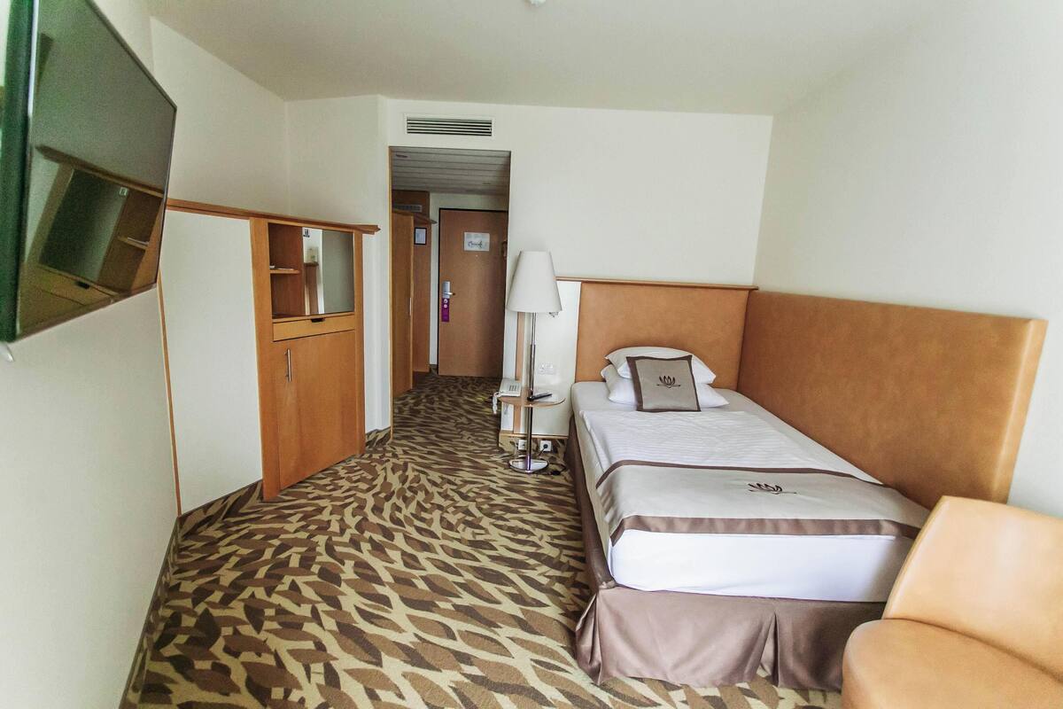 Ein Hotelzimmer mit zwei Betten, einem an der Wand befestigten Fernseher, einem Kleiderschrank und einem Spiegel.