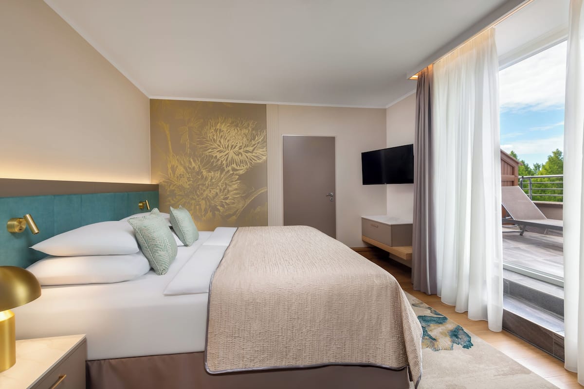 Ein modernes Hotelzimmer mit einem großen Bett, einem an der Wand montierten Fernseher und einem Balkon mit Blick ins Freie.