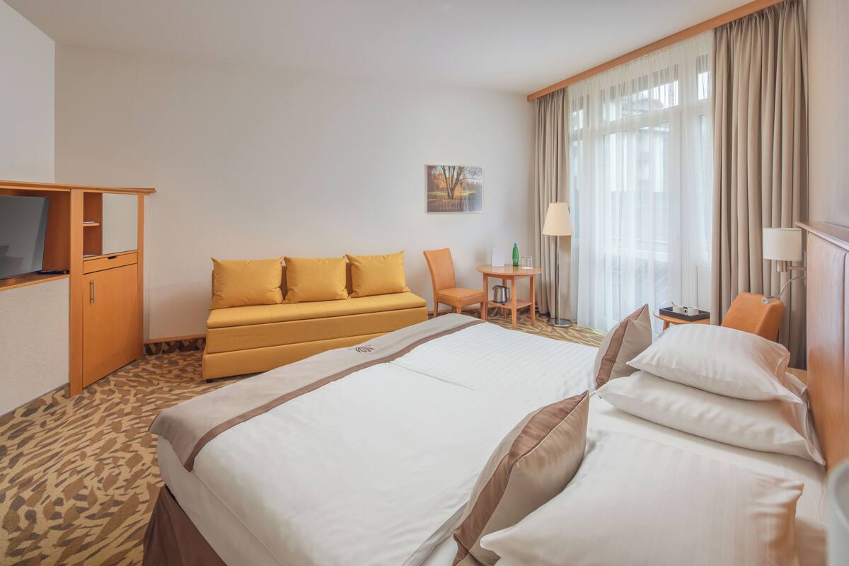 Ein Hotelzimmer mit einem großen Bett, einem Sofa, einem Fernseher, einem Schreibtisch und einem Sessel.