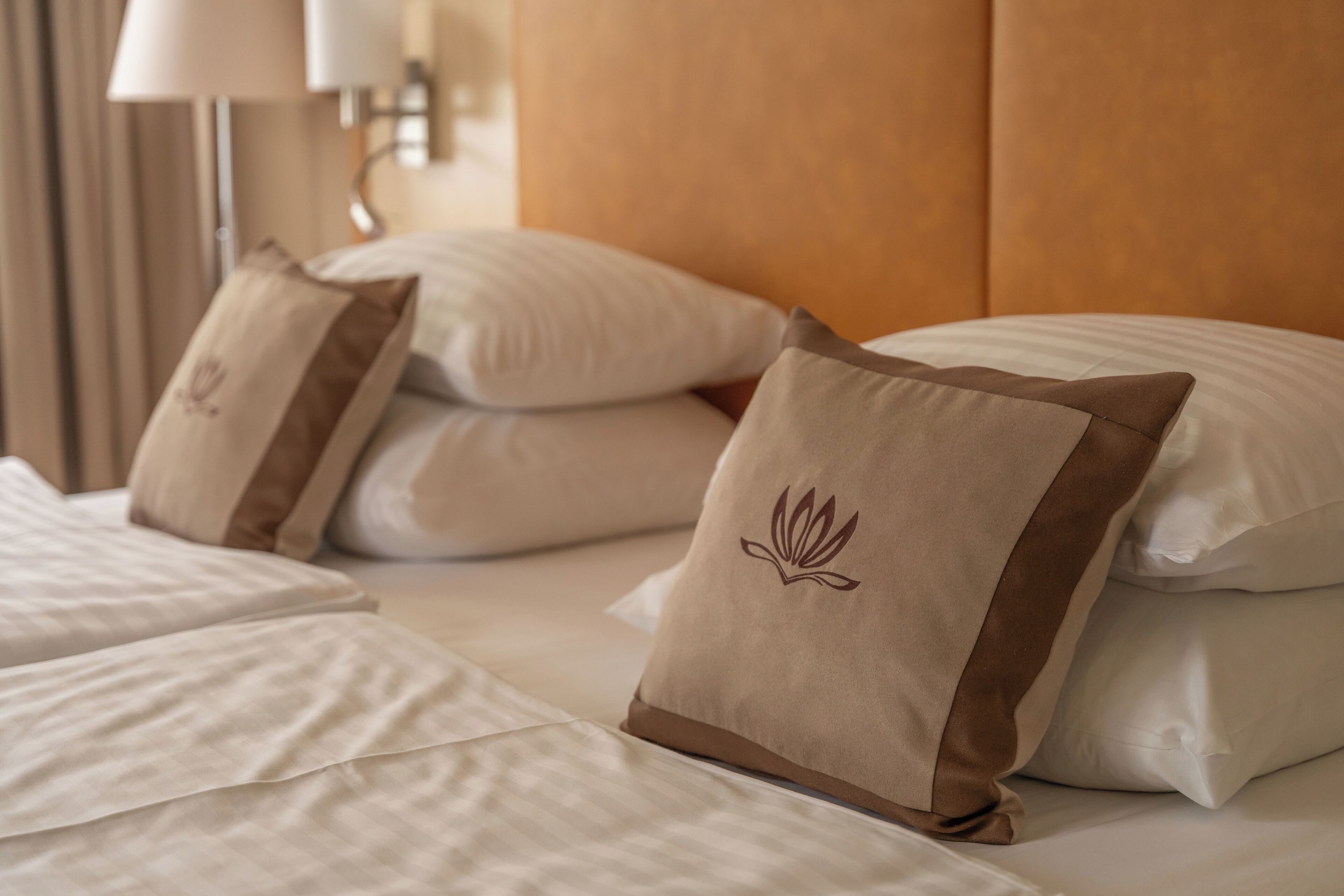 A neatly made bed with white linens and brown pillows with a floral design.