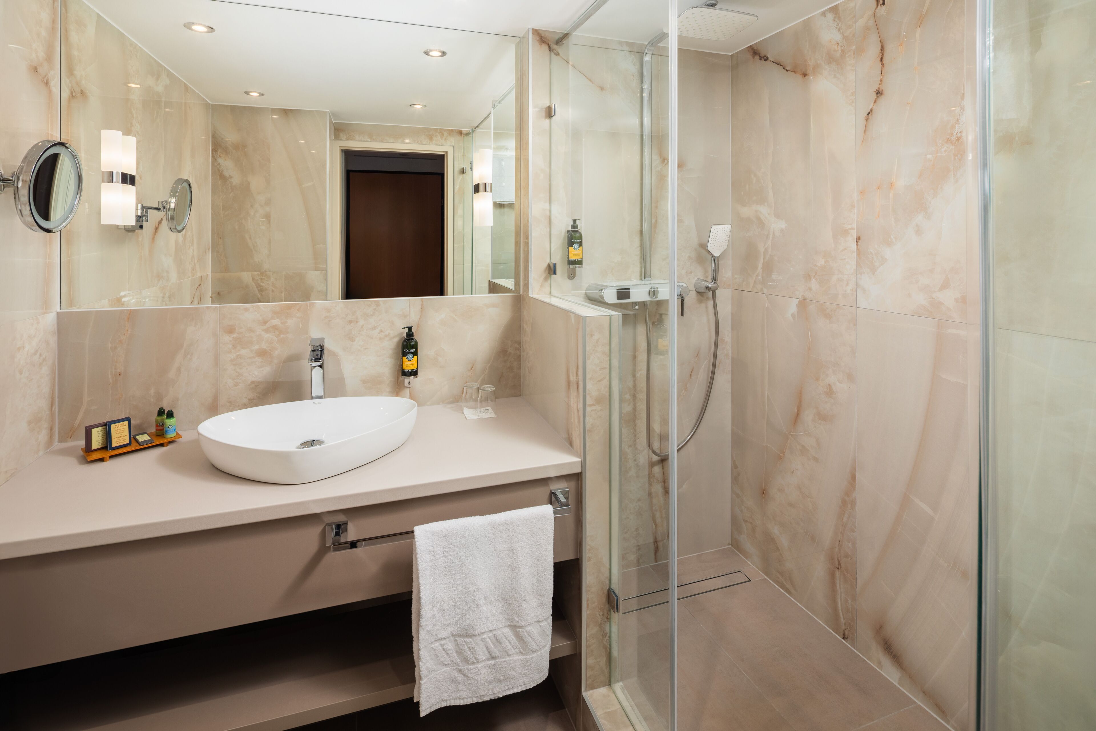 Un baño moderno con un espejo grande, un lavabo blanco y una ducha con mampara de vidrio.