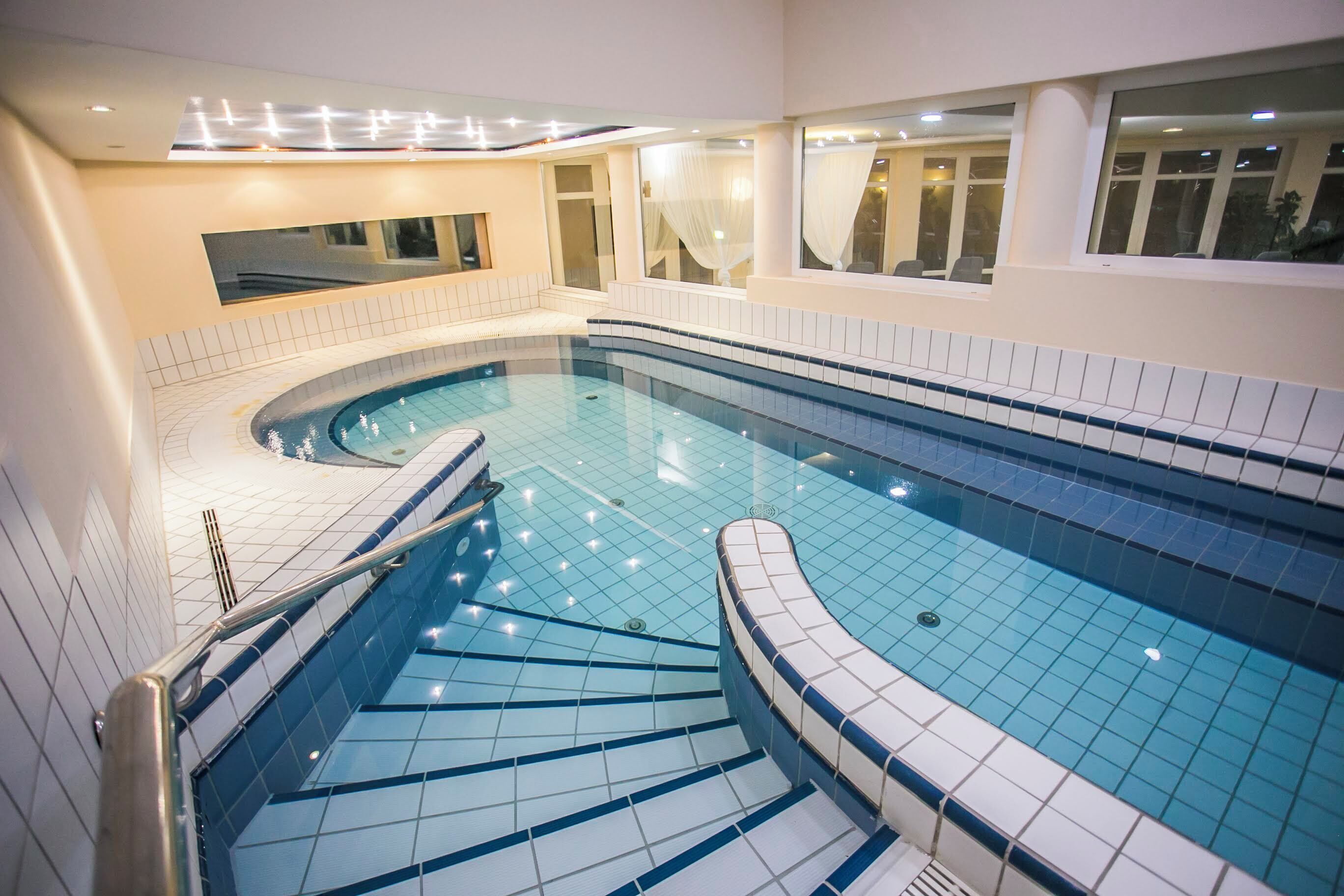 Una piscina interior moderna con diseño curvo, paredes enlosadas y una escalera que baja a la piscina.