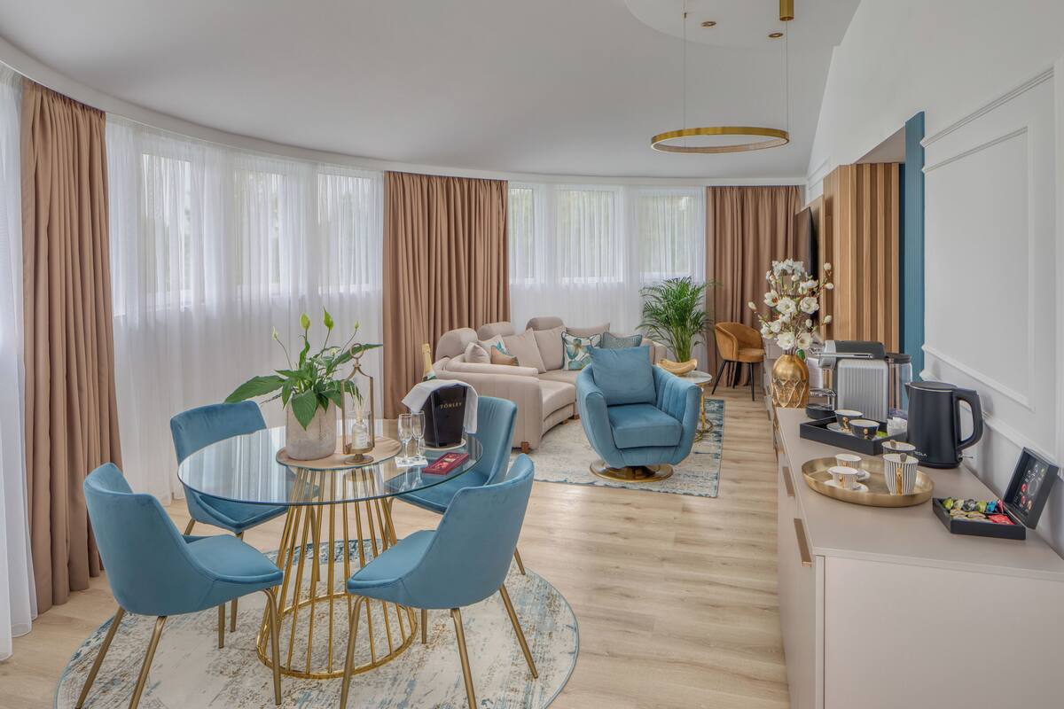 Ein modernes Wohnzimmer mit einem runden Glastisch, blauen Stühlen, einem beigen Sofa und einem Couchtisch.