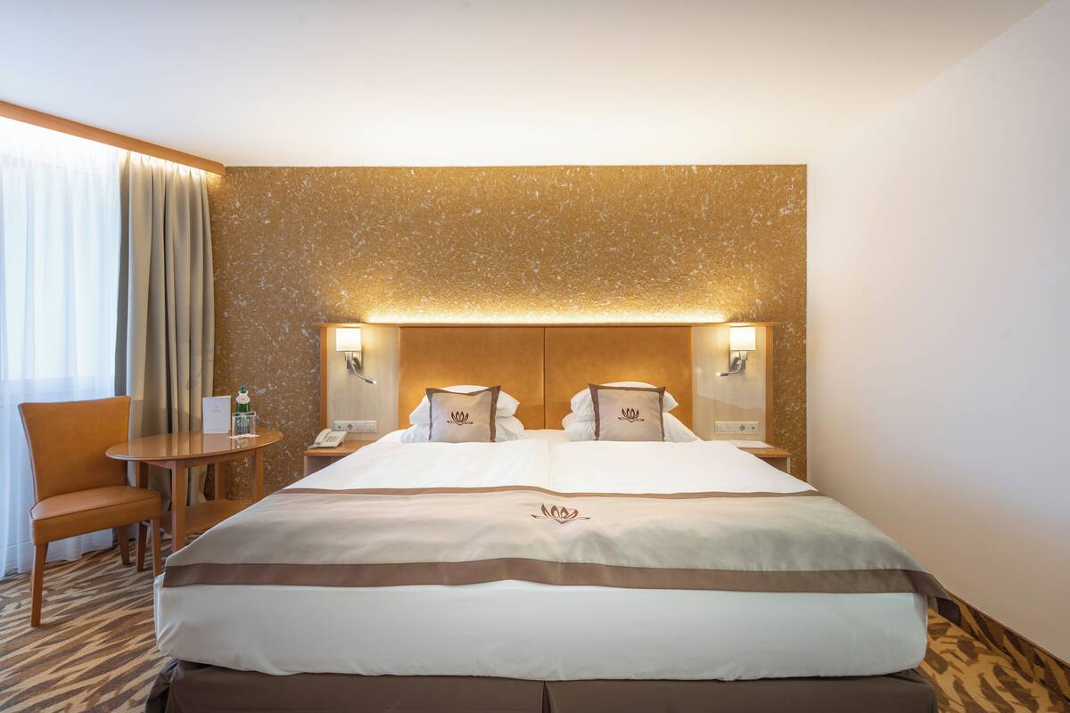 Ein Hotelzimmer mit einem großen Bett, zwei Nachttischen, einem Sessel und einem kleinen Tisch.