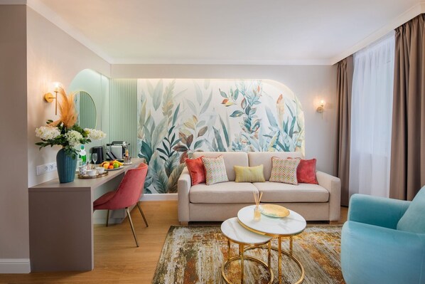 A modern living room with a sofa, a coffee table, and a dining area with a mirror and a vase of flowers.