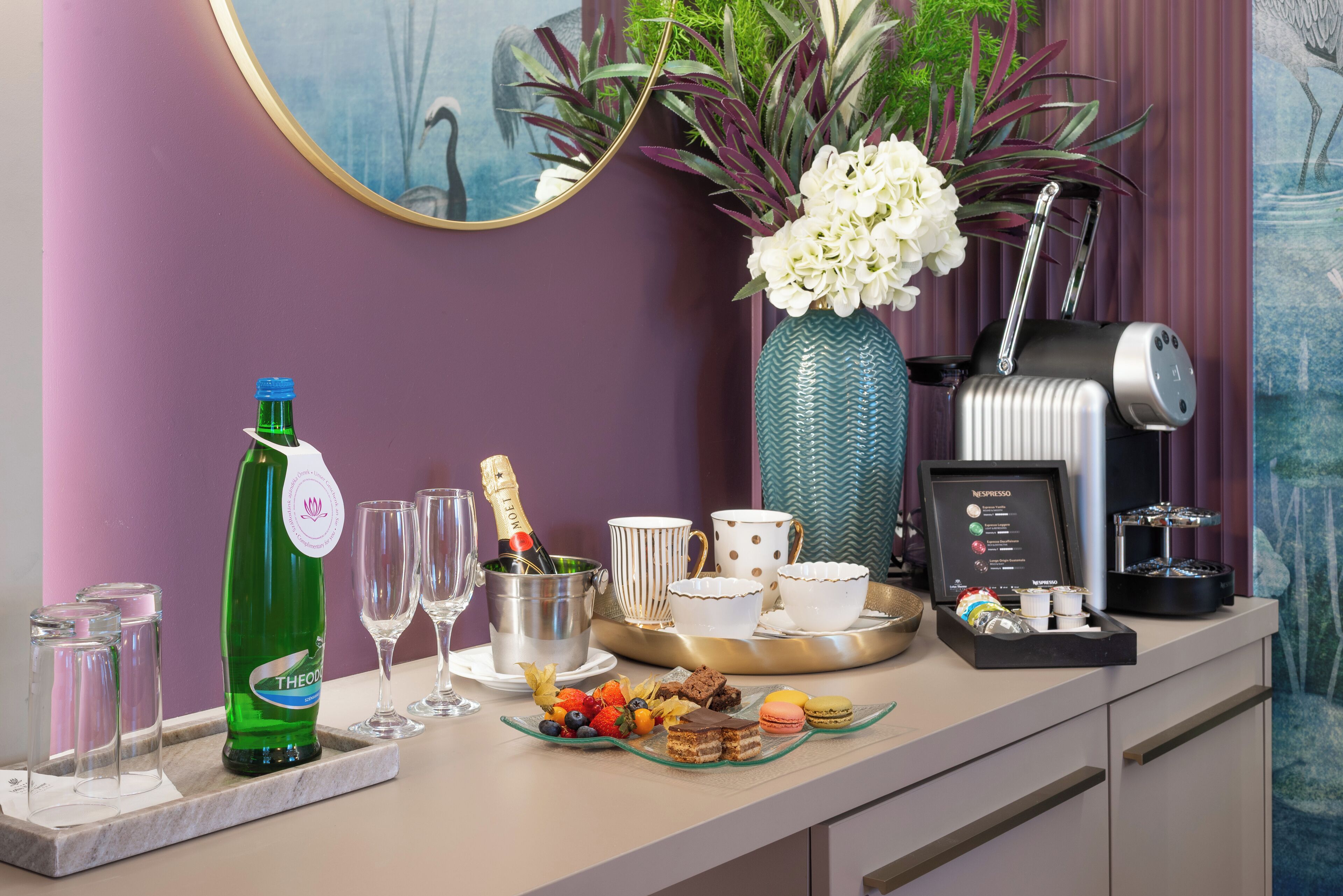 Ein liebevoll angerichteter Frühstückstisch mit einer Champagnerflasche, Gläsern, einer Auswahl an Gebäck und einer Kaffeemaschine.