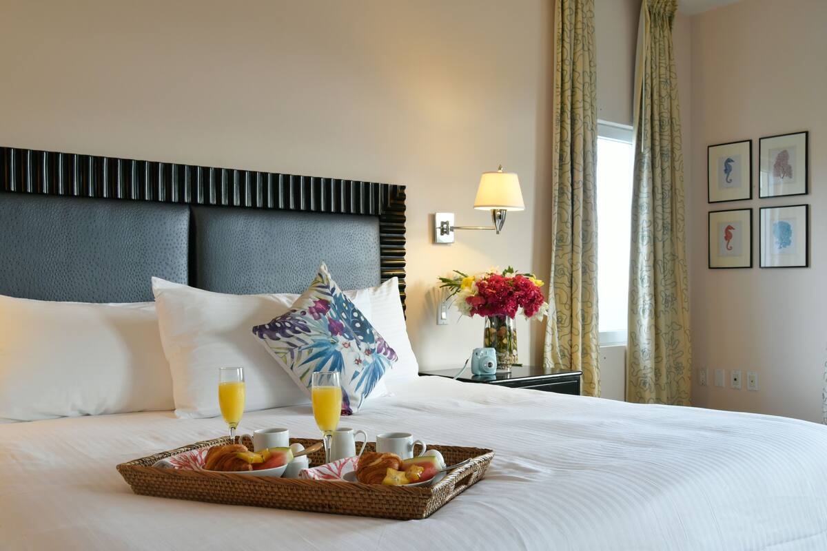 Un lit bien fait, avec un plateau contenant divers éléments pour le petit-déjeuner, notamment des croissants, des fruits et du jus, dans une chambre d’hôtel.
