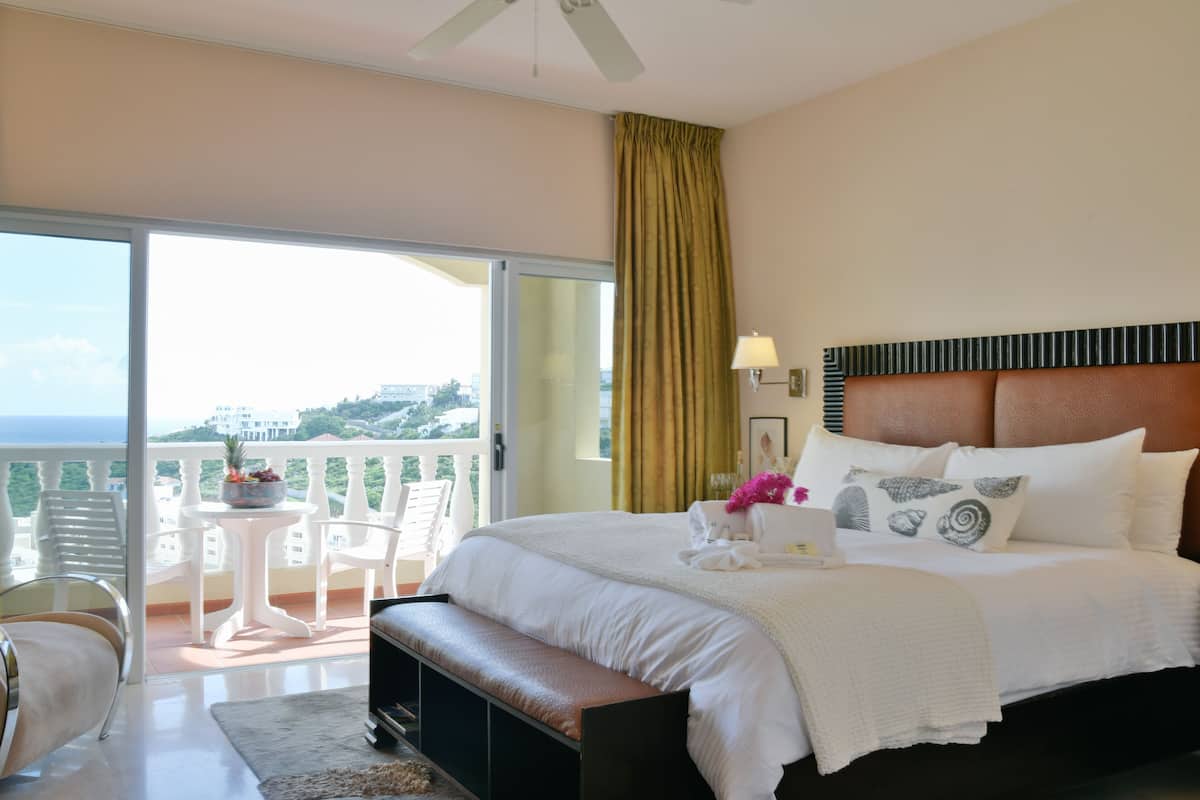 Une chambre d’hôtel avec un grand lit, un banc, une petite table avec des chaises et un balcon avec vue.