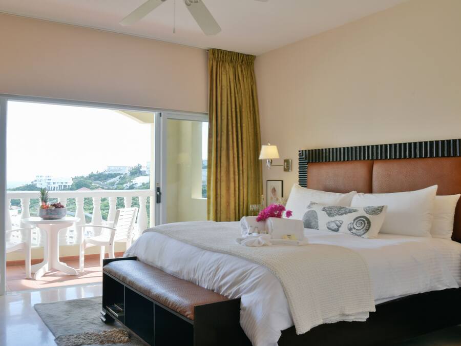 Une chambre d’hôtel avec un grand lit, un banc, une petite table avec des chaises et un balcon avec vue.