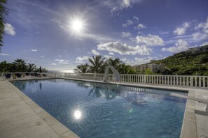 A clear blue pool with a white deck and palm trees, surrounded by a white fence and buildings in the background. - Princess Heights Luxury Boutique Condo Hotel (Oyster Pond)