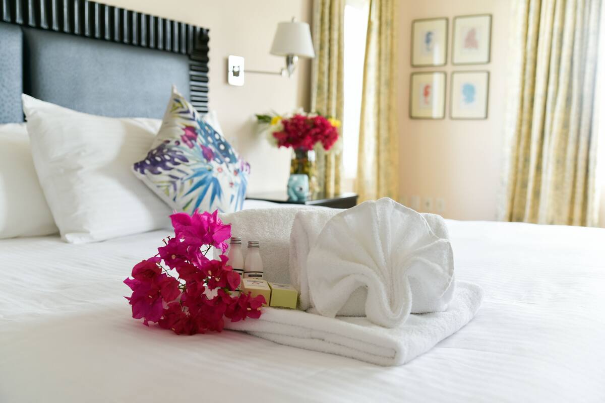 Un lit bien fait, avec une serviette blanche, un bouquet de fleurs roses et des articles de toilette.