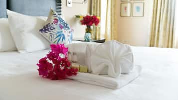 A neatly made bed with a white towel, a bouquet of pink flowers, and toiletries.