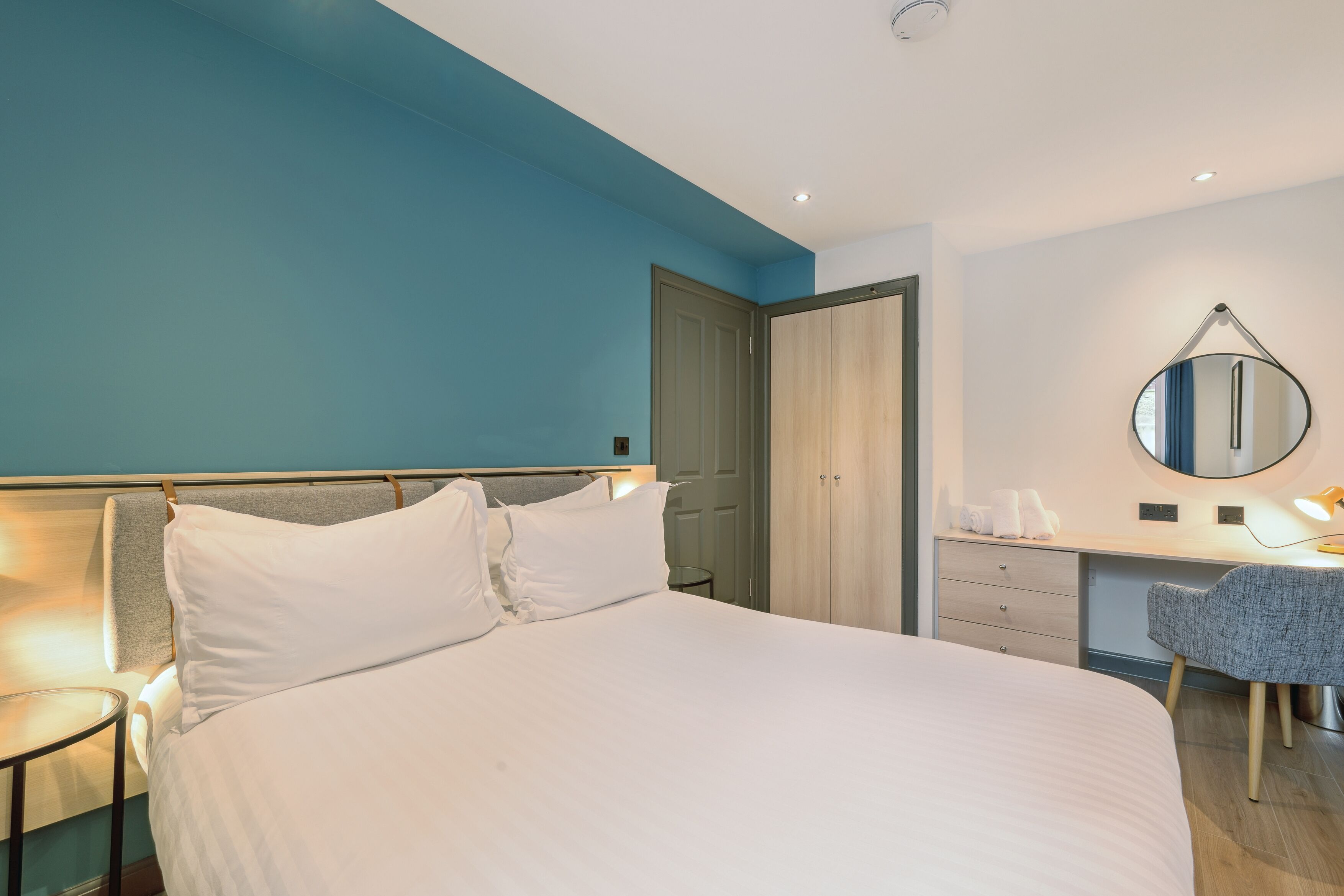 A hotel room with a large bed, a desk with a chair, a mirror, and a wardrobe.
