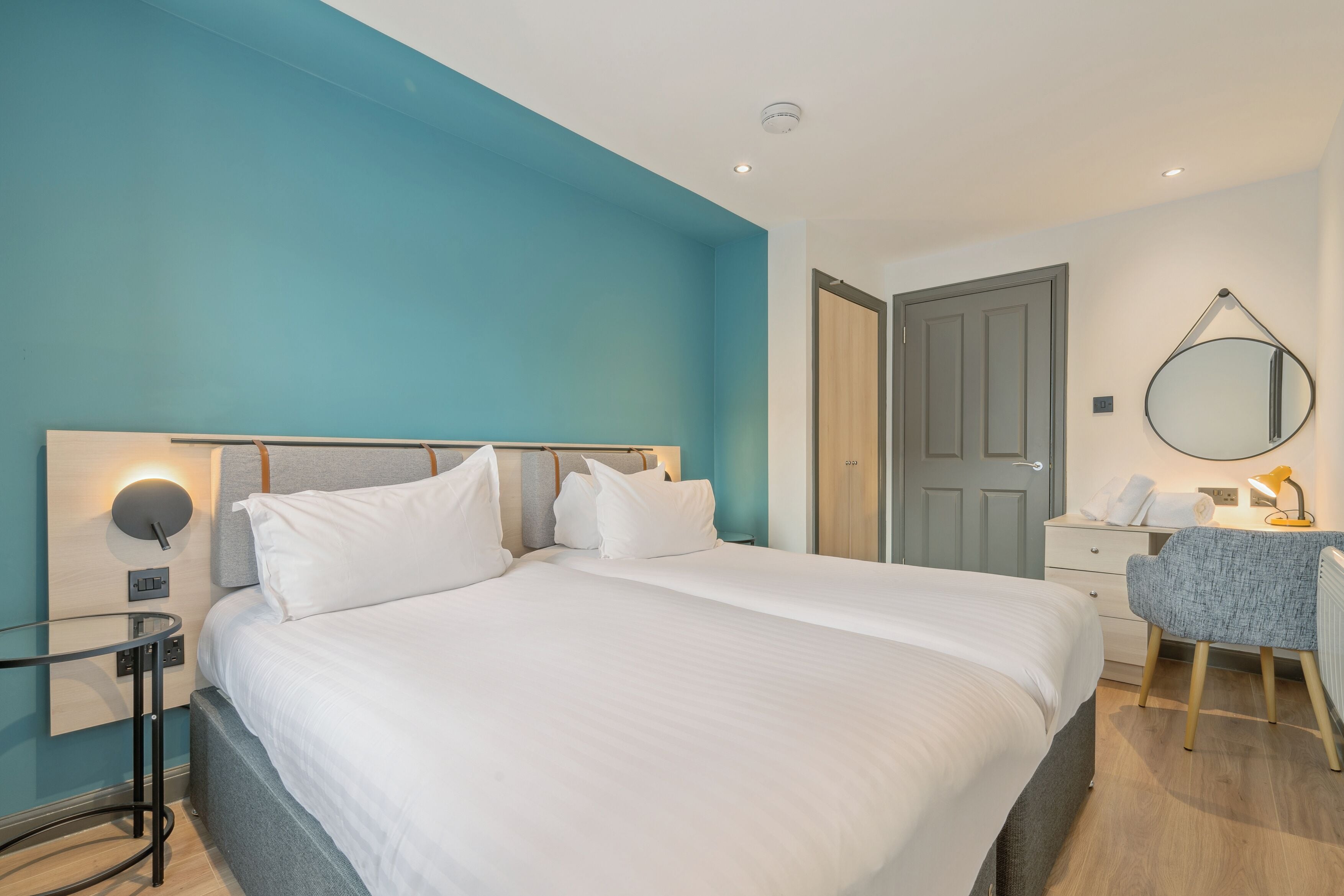 Una camera d'albergo moderna con un letto grande, una scrivania con sedia, uno specchio e una porta.