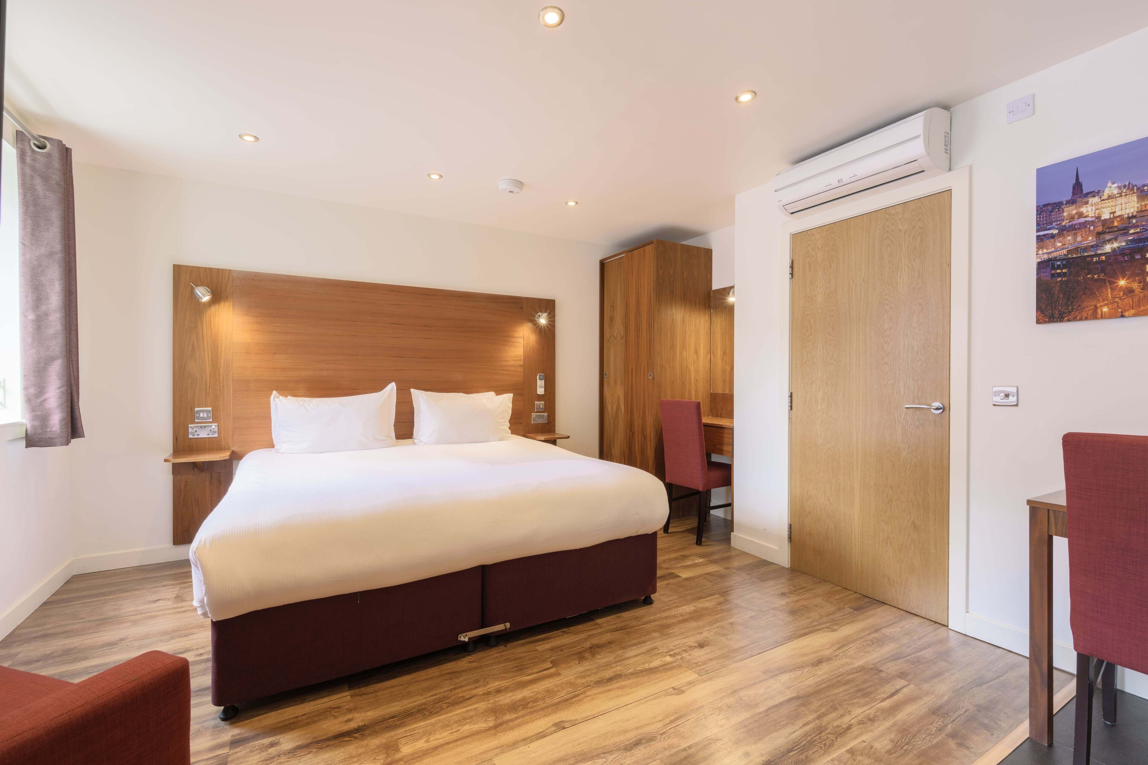 Een hotelkamer met een groot bed, een houten hoofdeinde, een bureau, een stoel en een kledingkast.