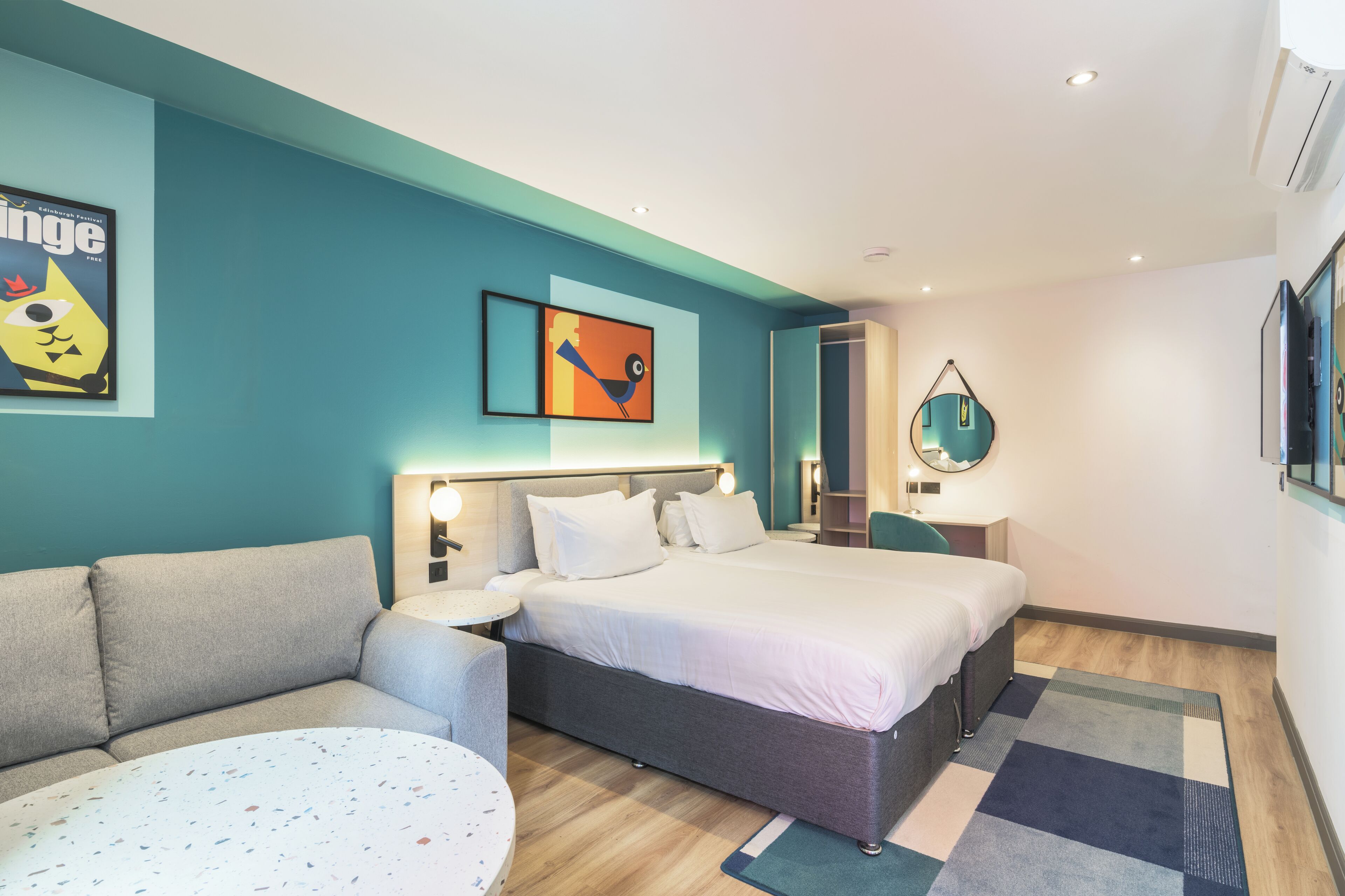 A modern hotel room with a large bed, a sofa, a small round table, and artwork on the walls.