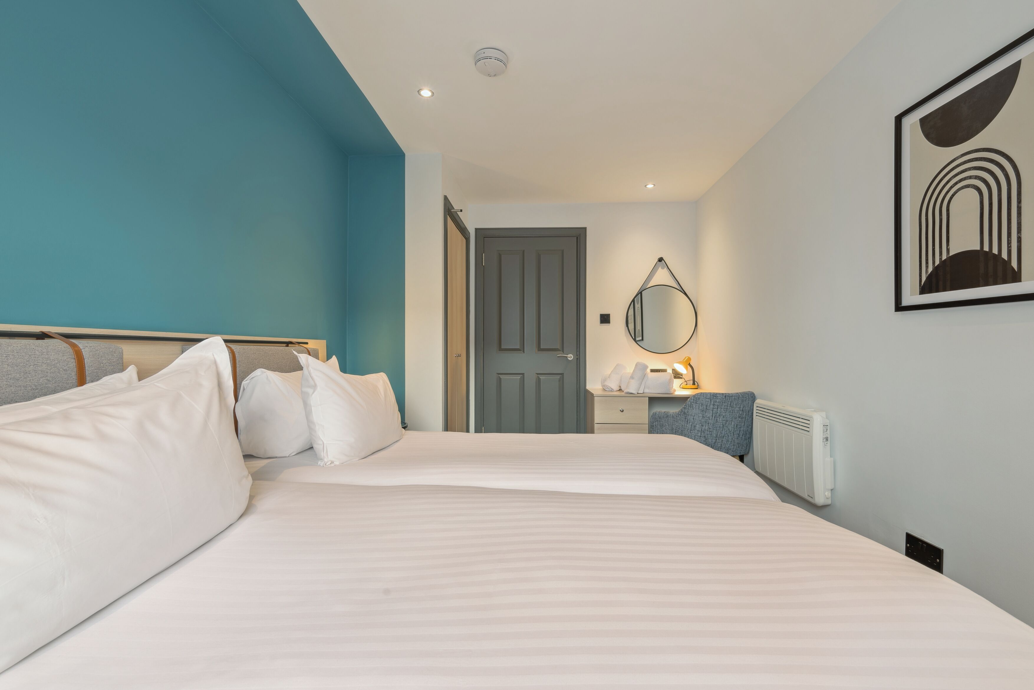 Une chambre d’hôtel avec un grand lit, une table de chevet avec une lampe, un miroir et un radiateur.