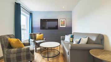 Una sala de estar moderna con un sofá gris, dos sillones, una mesa de centro y un televisor de pantalla plana montado en la pared.