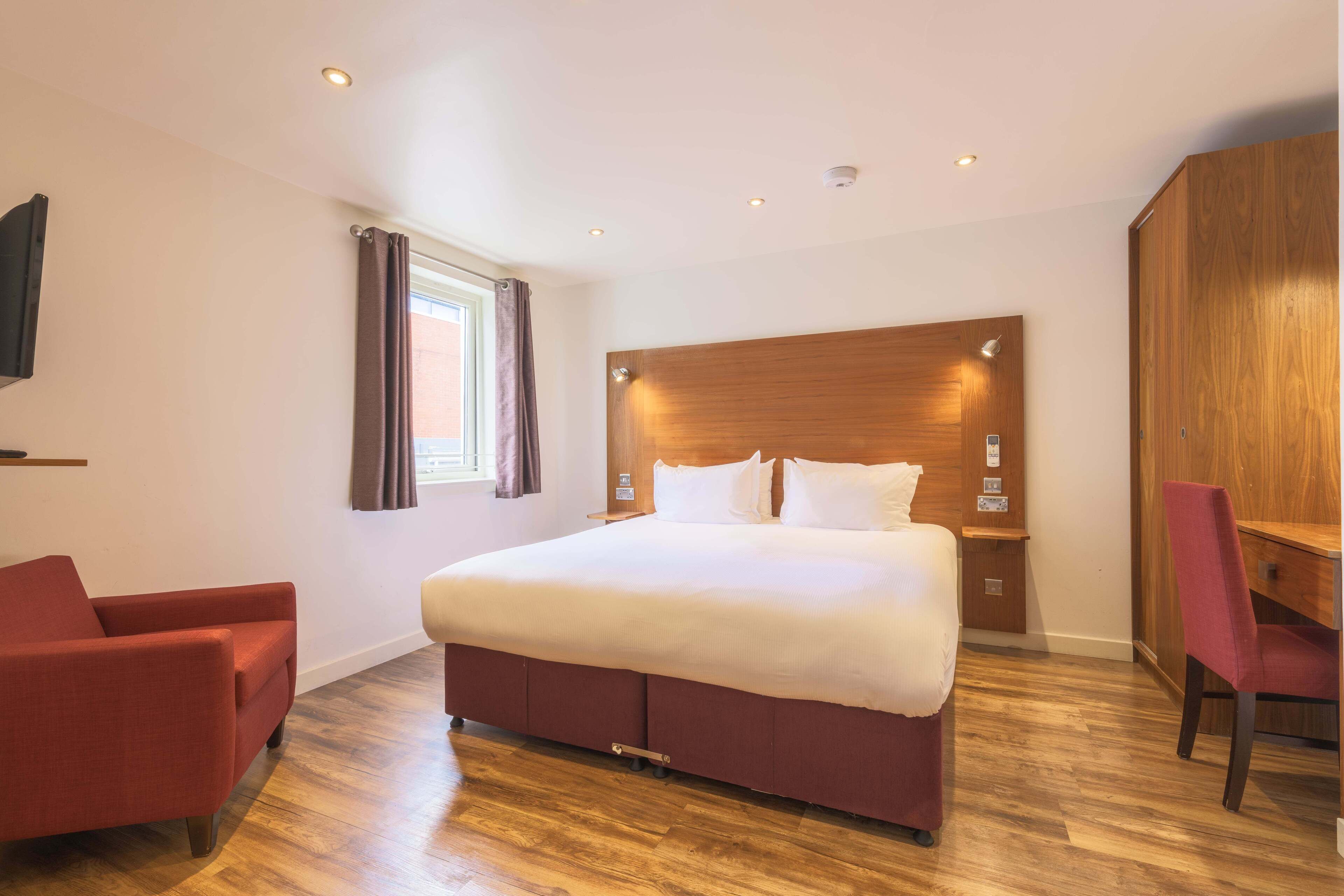 A hotel room with a large bed, a desk, a chair, and a TV mounted on the wall.